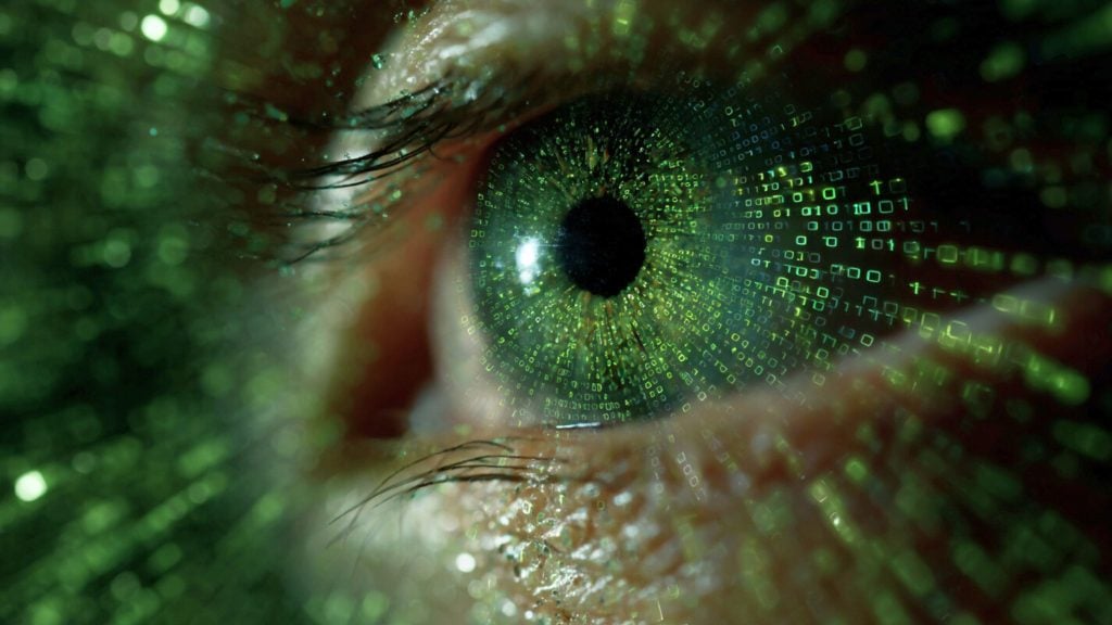 Close-up of a human eye with green digital binary code superimposed over the iris, creating a futuristic and technological effect.