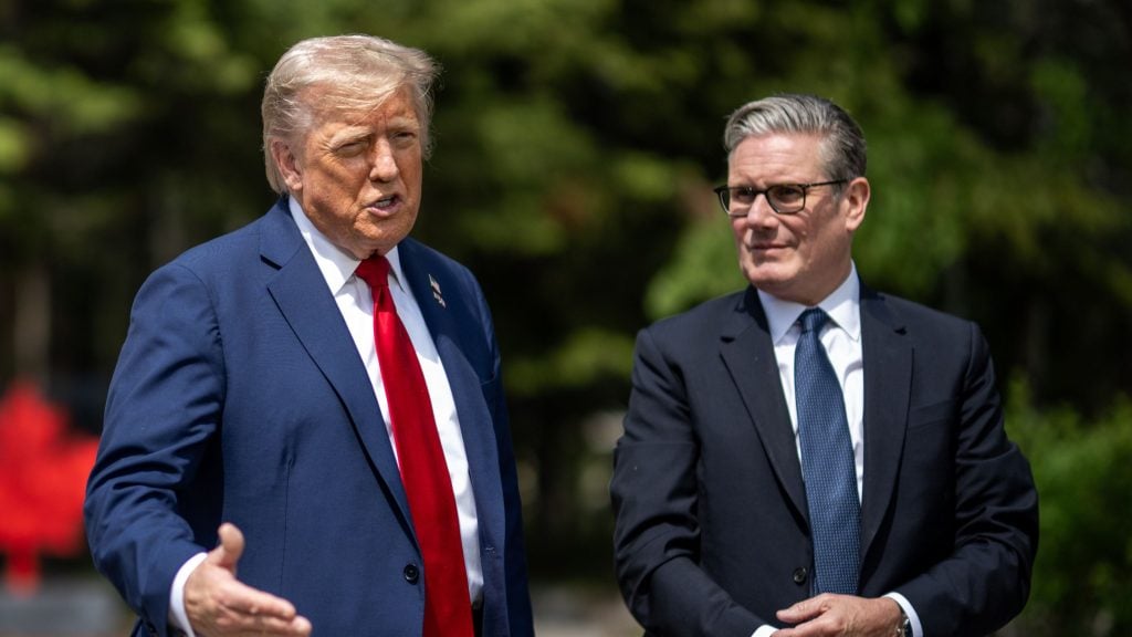 Trump and Starmer standing outdoors; the man on the left in a navy suit and red tie is gesturing while speaking, and the man on the right wears glasses and a dark suit with a blue tie, listening.