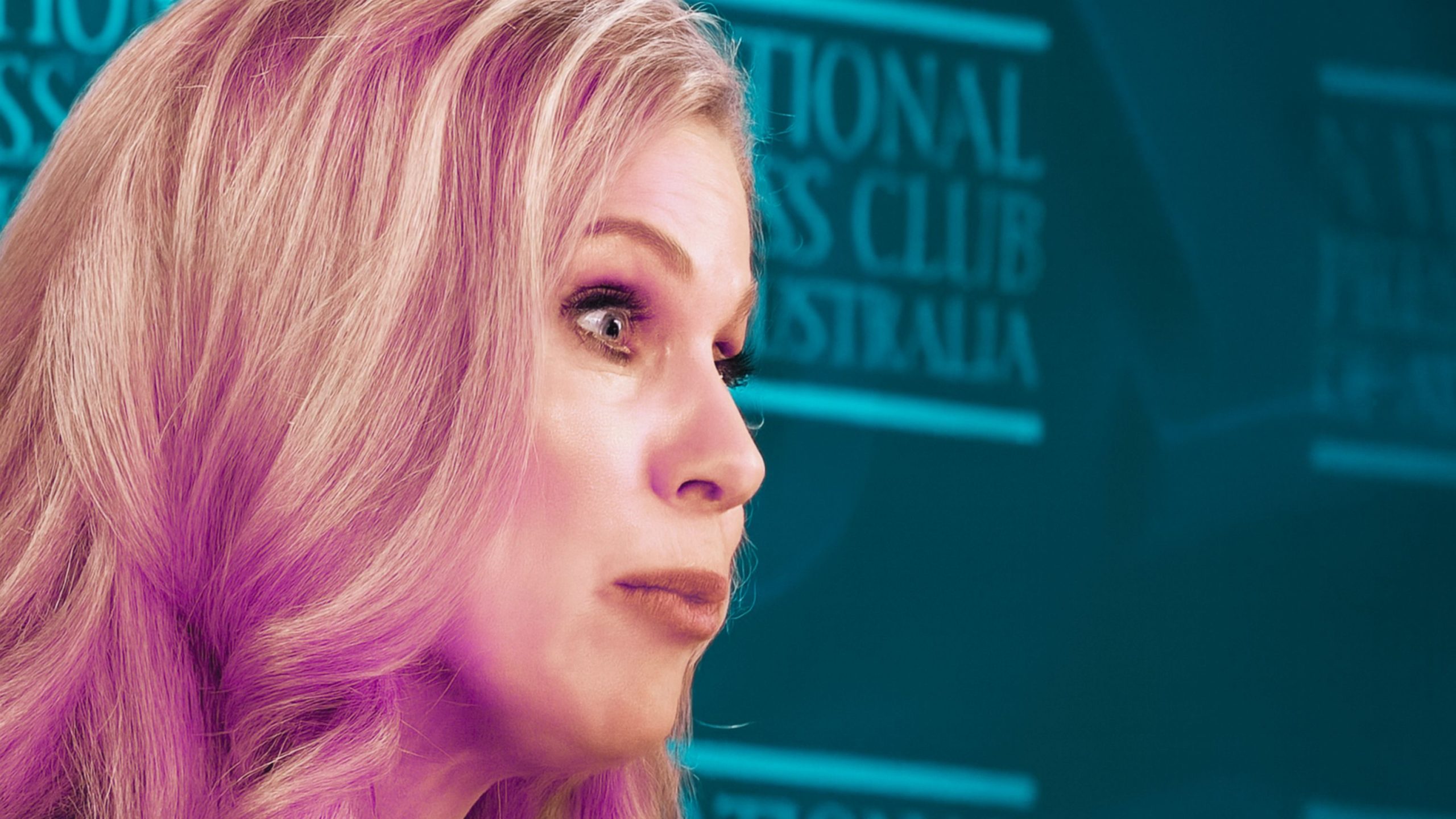 Close-up profile Inman Grant with long wavy hair and expressive eyes, pursing her lips as she speaks in front of a teal backdrop with blurred 'National Press Club Australia' text.