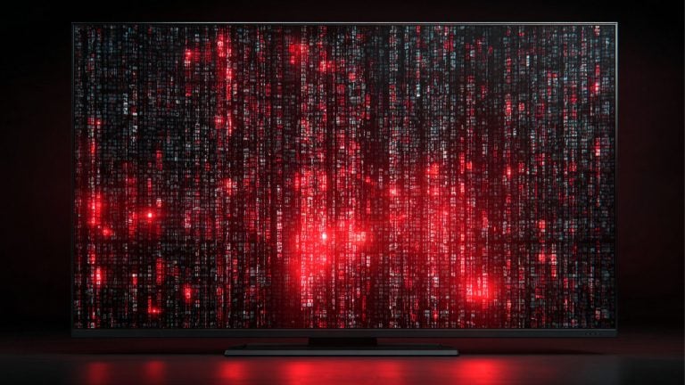 Flat-screen television displaying dense vertical columns of red and blue pixelated code with bright red glowing clusters, set against a dark background with a red reflection on the surface below