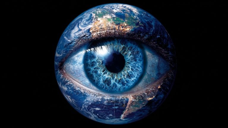 Surreal composite of the Earth as a giant blue human eye, with continents and city lights forming the eyelids and a vivid detailed iris at the globe's center against a black space background.