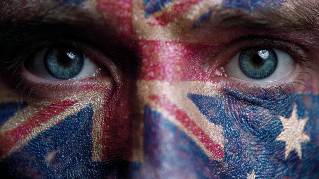 Extreme close-up of a person's face with the Australian flag painted across the nose and cheeks, showing textured blue and red paint, white stars and vivid blue irises.