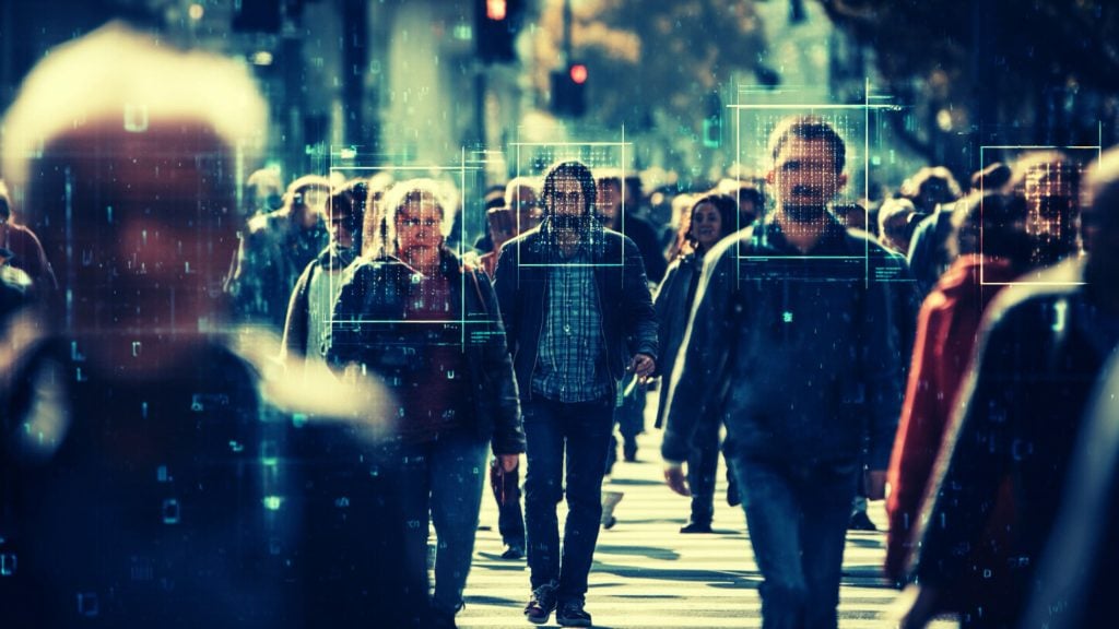 People walking on a busy city sidewalk in daylight, with several faces framed by glowing rectangular facial-recognition boxes and a semi-transparent digital code overlay across the scene.