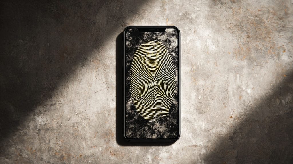 Smartphone centered on a rough concrete surface displaying a large yellow fingerprint on its screen, with diagonal shadows falling across the background.