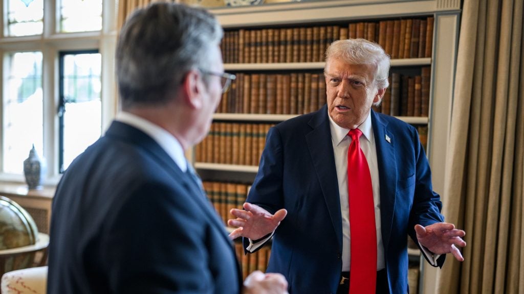 Trump in a navy suit and red tie gesturing while speaking to Starmer in a book-lined office.