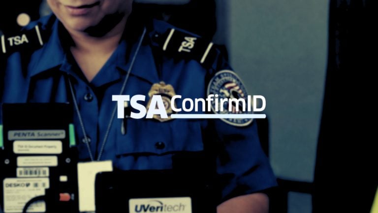 TSA officer in blue uniform with badge and shoulder "TSA" patches holding an ID scanner, overlaid text "TSA ConfirmID".