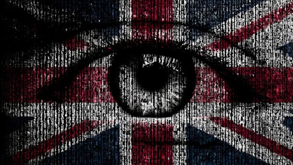 A large close-up eye in grayscale is centered over a Union Jack flag, with vertical columns of white alphanumeric code overlaying the red, white and blue background to create a digital surveillance effect.