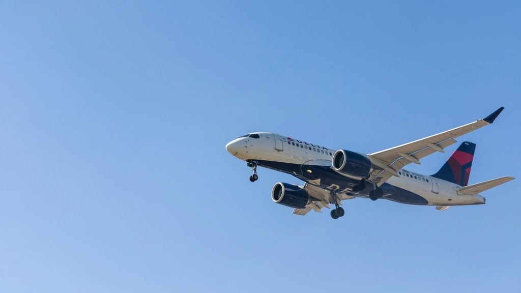 Delta Air Lines passenger jet descending with landing gear deployed against a clear blue sky.