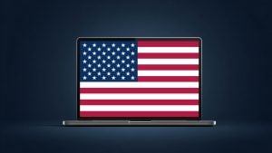 Silver laptop on a dark blue background displaying a full-screen United States flag on its screen.