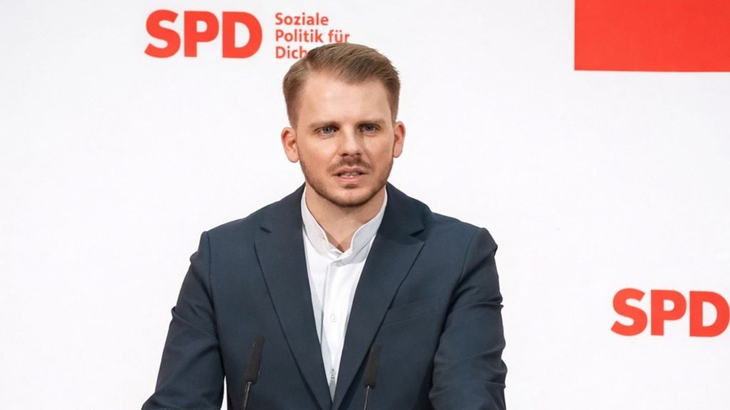 Klüssendorf in navy suit speaking at podium in front of SPD logo and slogan on a white background.