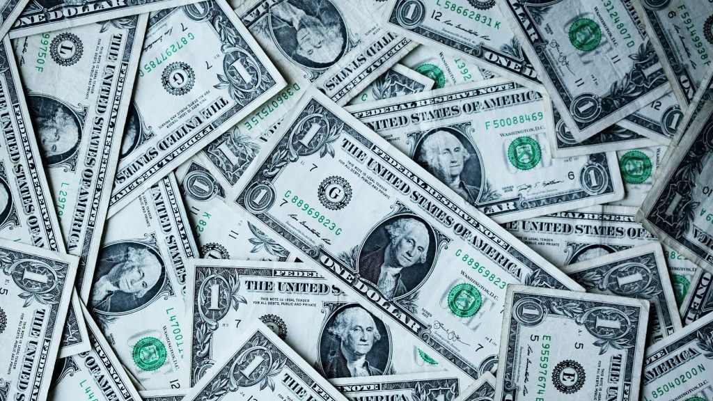 Close-up of overlapping United States one-dollar bills showing central portrait, large 1 numerals, and green Treasury seals.