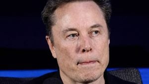 Close-up of Elon Musk with short dark hair, blue-gray eyes looking right and lips pressed together