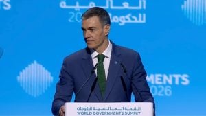 Pedro Sánchez in a dark suit and green tie speaking at a podium labeled World Governments Summit against a blue backdrop.