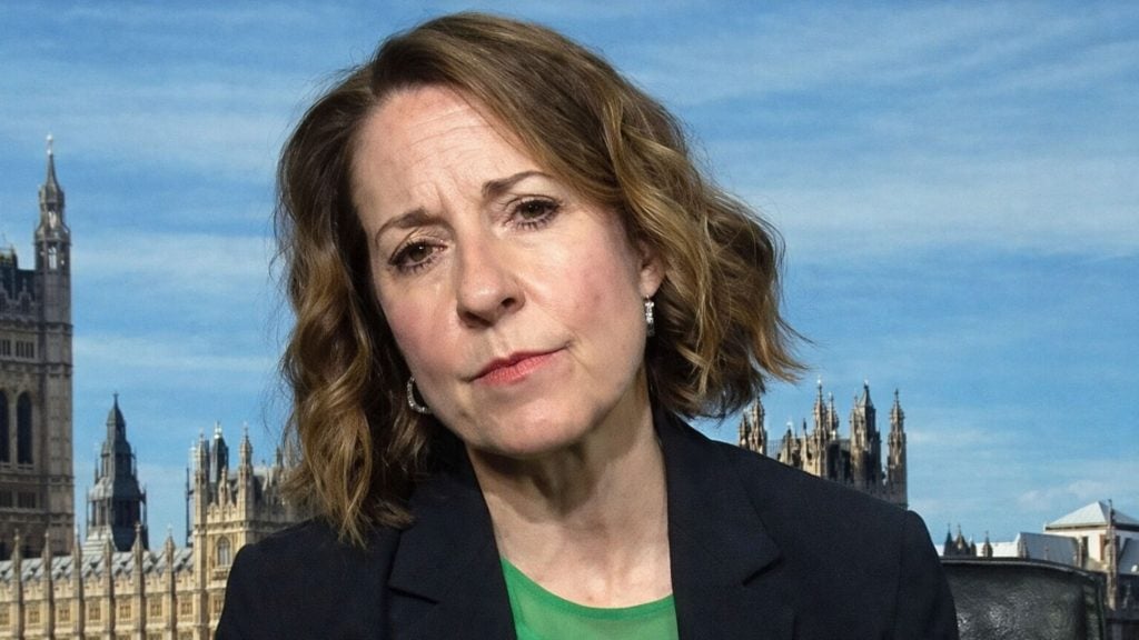 Kendall with wavy brown hair in a dark blazer and green top, Palace of Westminster buildings visible behind her.