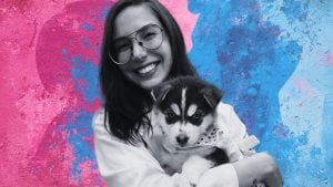 Borges in glasses holding a black-and-white husky puppy wearing a polka-dot bandana against a pink and blue wall