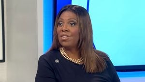 Letitia James with straight brown hair and wide-eyed expression wearing a double-strand pearl necklace and dark top against a blue studio background