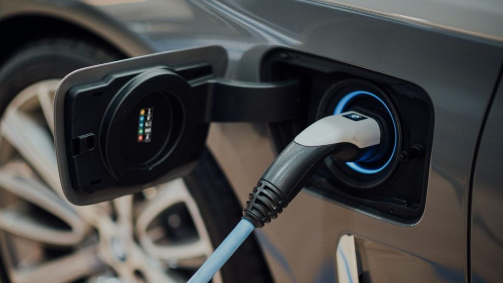 Electric vehicle charging port with a blue-ringed charging connector plugged into a gray car.