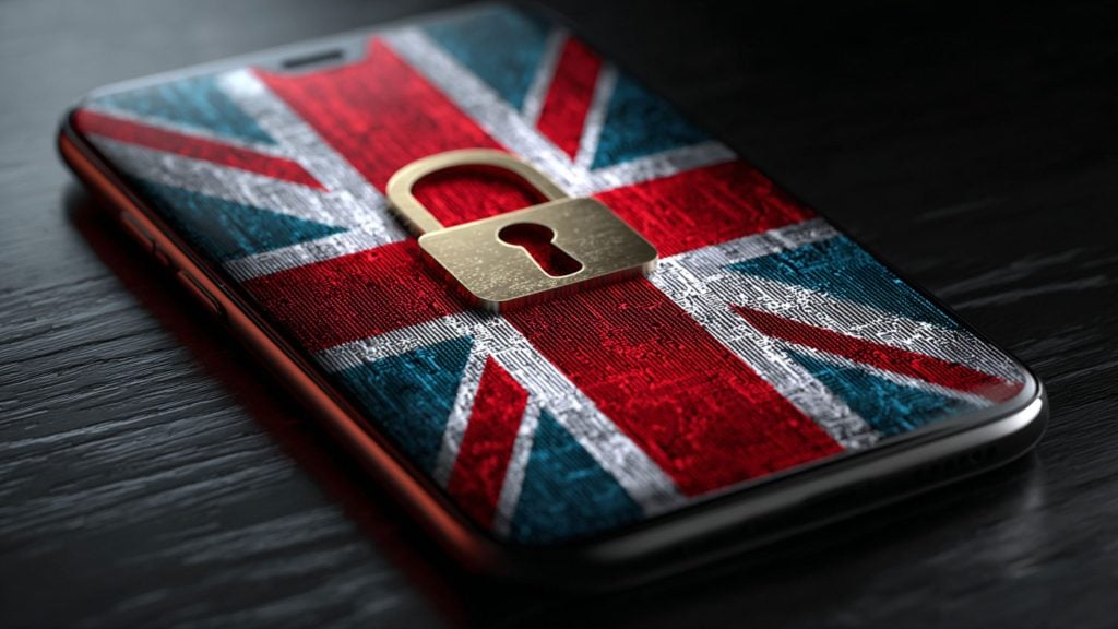 Smartphone lying on dark wood with a textured Union Jack wallpaper and a gold padlock icon centered on the screen.