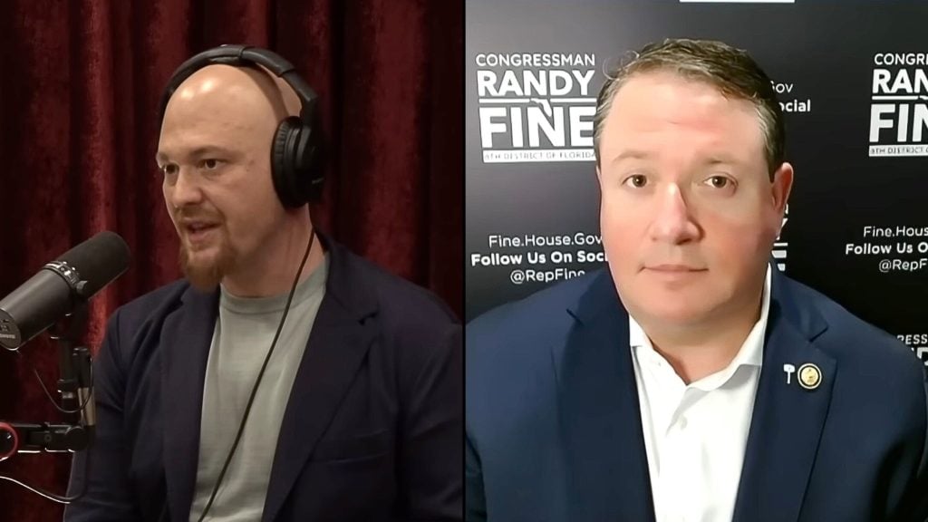 Split-screen interview: left, a bald man with headphones speaking into a microphone against red curtains; right, a suited man against a dark campaign-style backdrop with white text.