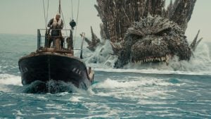 Fishing boat at sea with a terrified crewman at the helm as a giant spiky sea monster rises behind, baring teeth.