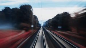 Blurred motion view down straight railroad tracks flanked by dark trees and red-tinged ground under a blue-gray sky