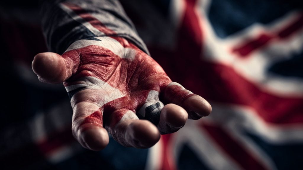Outstretched hand painted with the Union Jack flag, palm toward the viewer with blurred flag background
