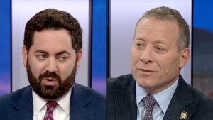 Gottheimer and Lawler, two men in suits during a TV discussion, left man with dark hair and beard, right man clean-shaven wearing a pin.